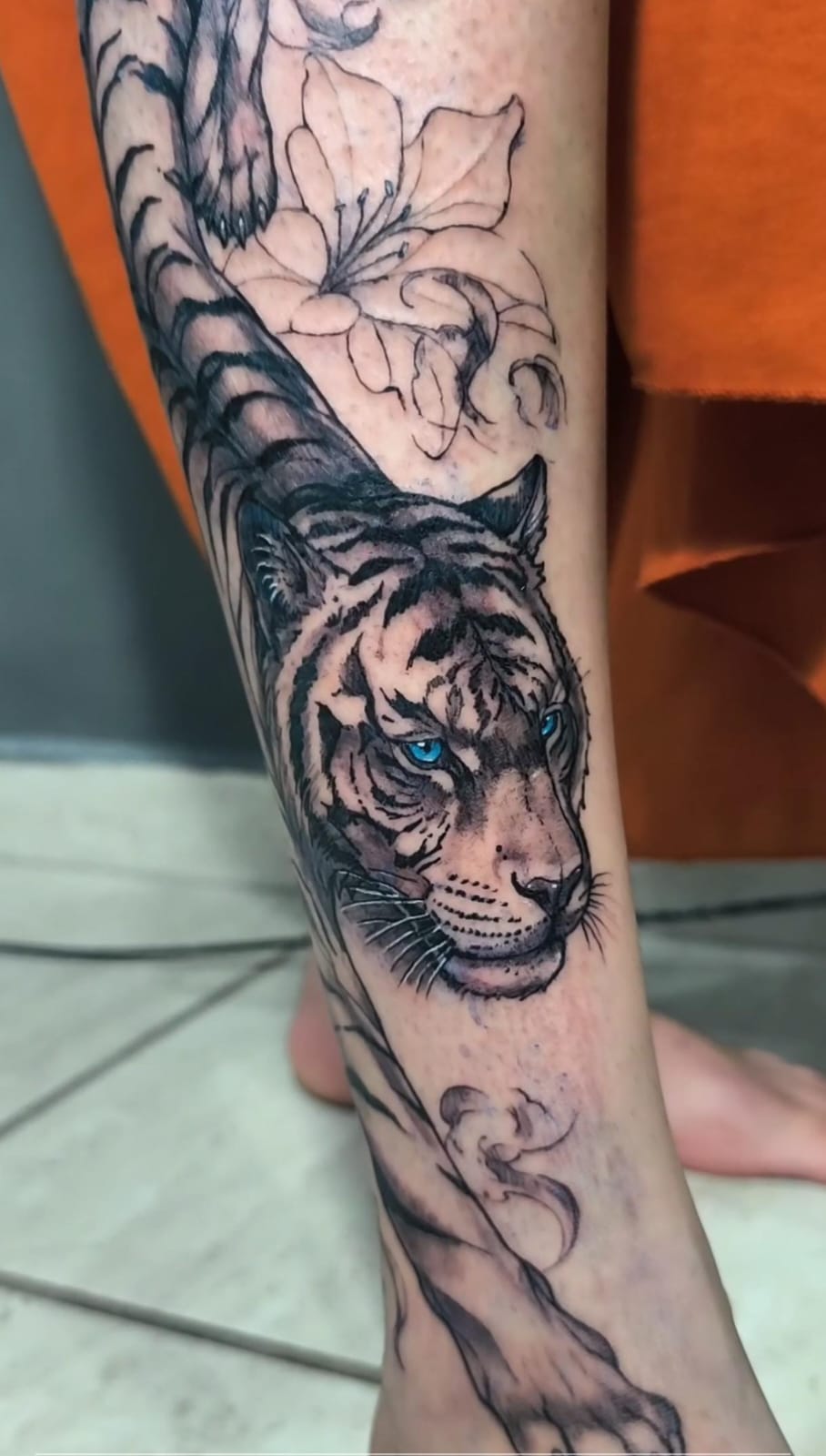 Tatuagem grande de tigre com flores na perna